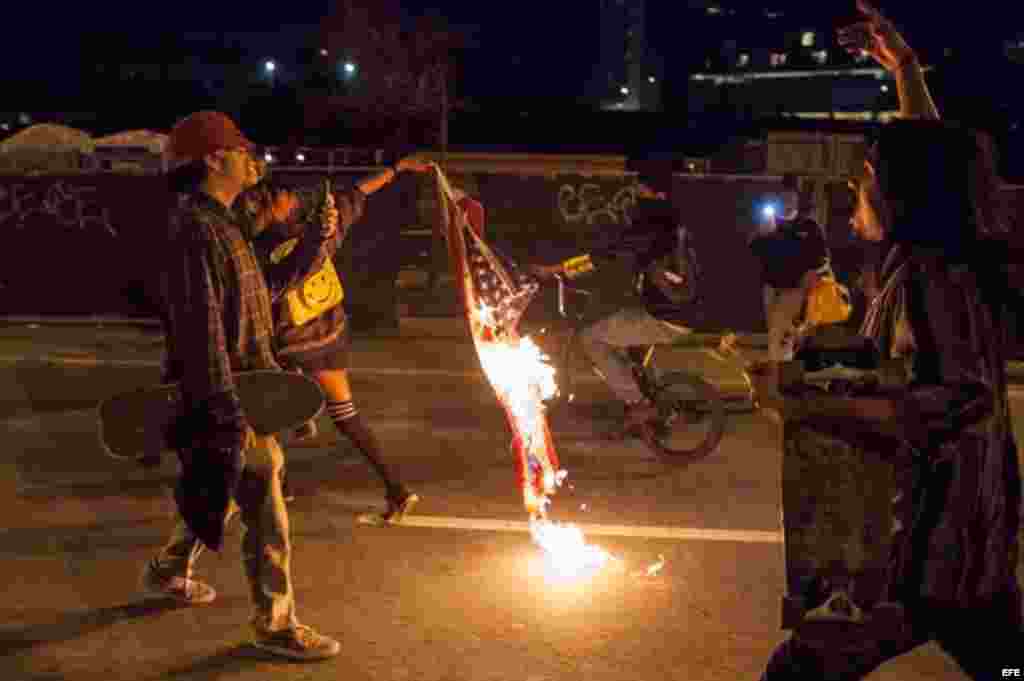 Un manifestante lleva una bandera estadounidense en llamas durante una protesta en Oakland, California (EEUU) contra la elección del republicano Donald Trump como nuevo presidente estadounidense. 