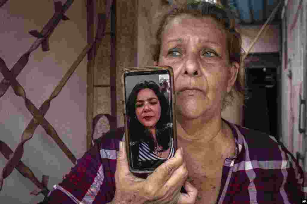 Yanelis Leon habla por videollamada desde Estados Unidos durante una entrevista mientras su madre, Natacha González, quien cuida de sus dos hijos, sostiene el celular en la entrada de su casa en Cienfuegos. (AP Foto/Ramón Espinosa)